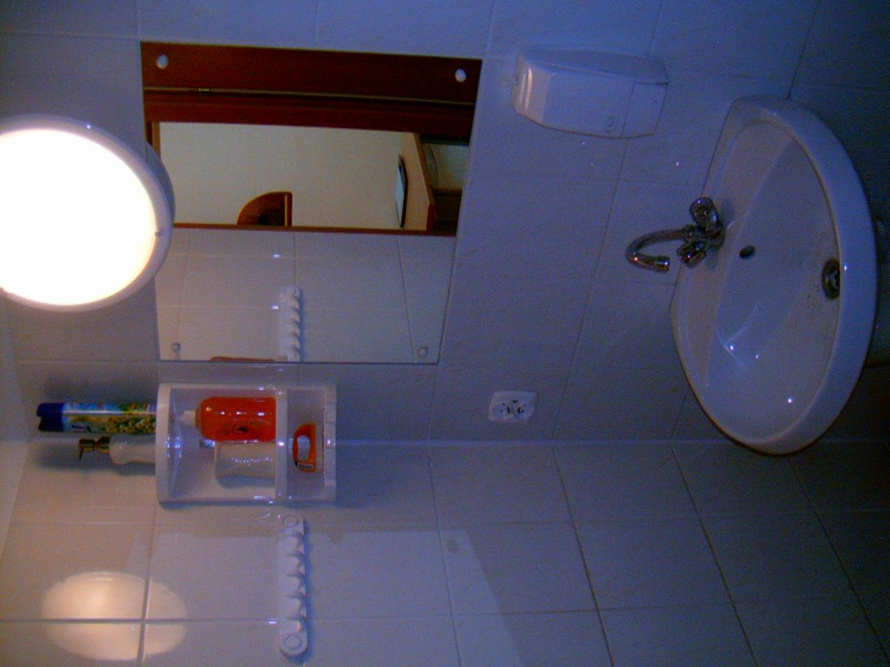 Łazienka w Warlubiu z białą umywalką, lustrem z drewnianą ramą i półką z kosmetykami, sfotografowana pod nietypowym kątem.