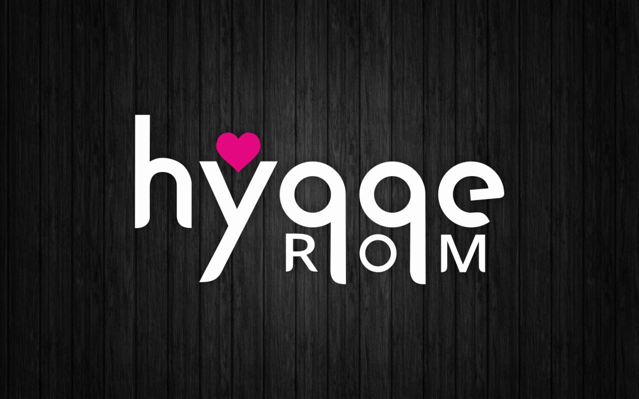 Białe logo 'hygge ROOM' z różowym sercem zamiast kropki nad 'i' na tle ciemnego, drewnianego panelu.