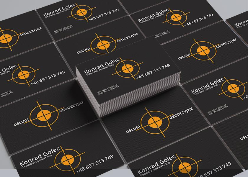 Stos wizytówek na ciemnym tle. Wizytówki w kolorze czarnym z pomarańczowym logo celownika, danymi kontaktowymi i informacją o geodecie uprawnionym.