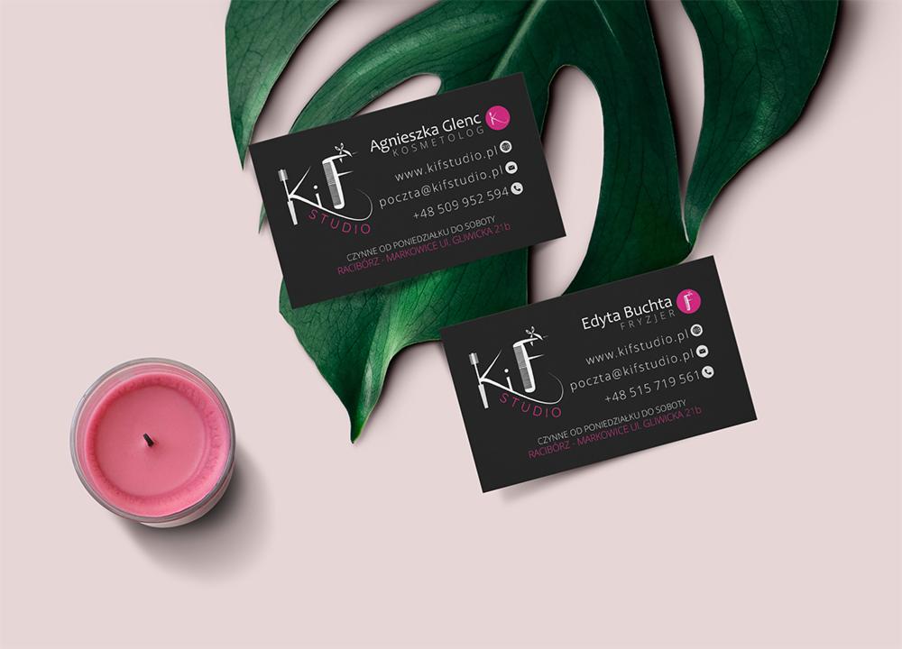 Dwie czarne wizytówki Kif Studio z logo i danymi kontaktowymi kosmetyczki Agnieszki Glenc i fryzjerki Edyty Buchty, leżące na tle liścia monstery i różowej świecy.