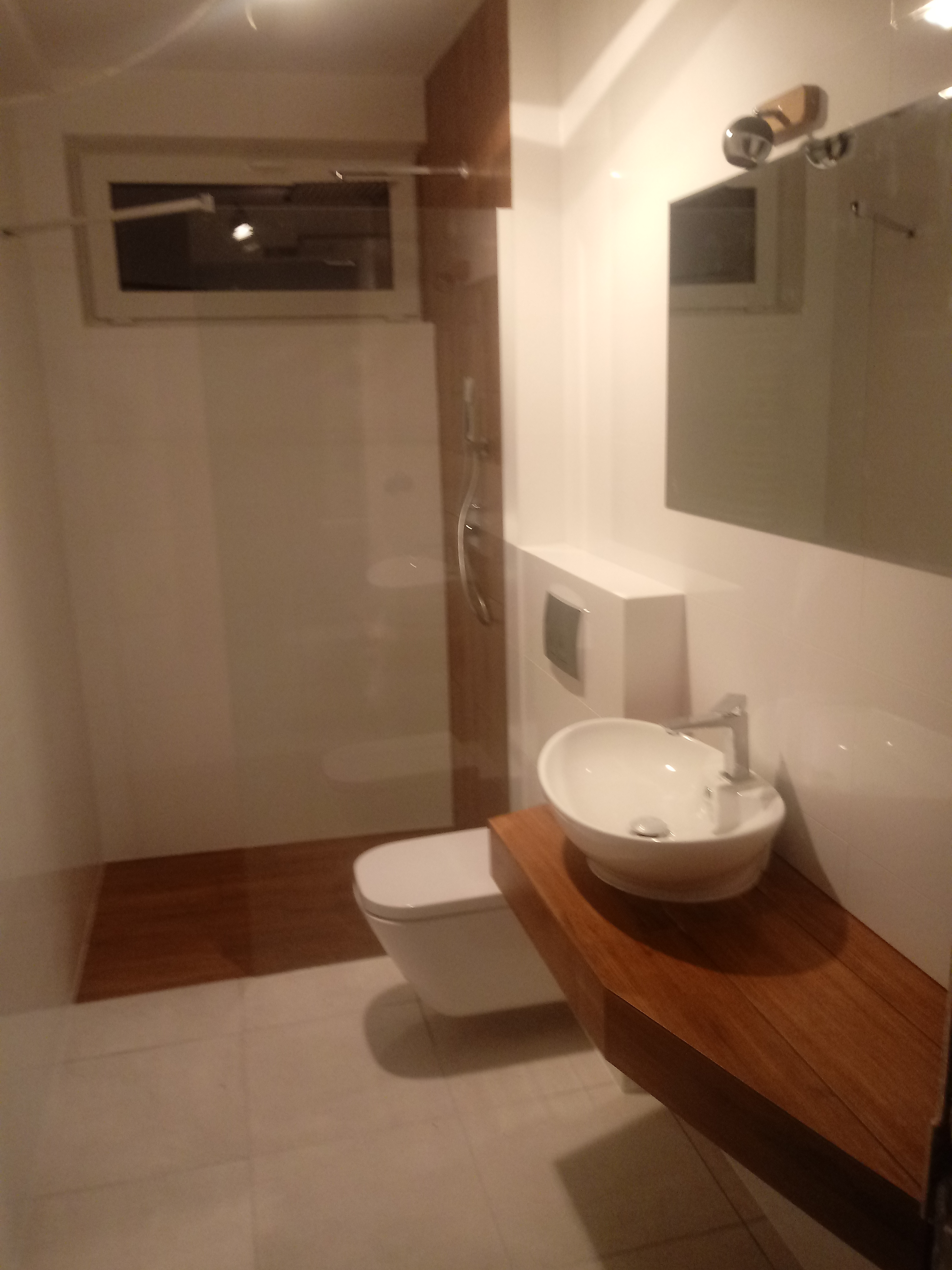 Nowoczesna łazienka z kabiną prysznicową typu walk-in, podwieszaną toaletą i umywalką nablatową na drewnianym blacie.