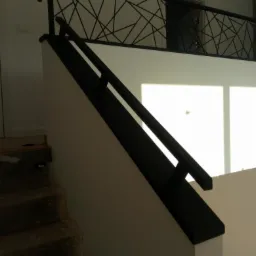 Nowoczesne schody z czarną, geometryczną balustradą metalową, widok z dołu na jasne wnętrze.