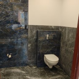 Rad-Bud - Wykończona łazienka z marmurowymi płytkami w odcieniach szarości i bieli. Wisząca toaleta, minimalistyczny design, oświetlenie punktowe. Widok zza framugi drzwi.