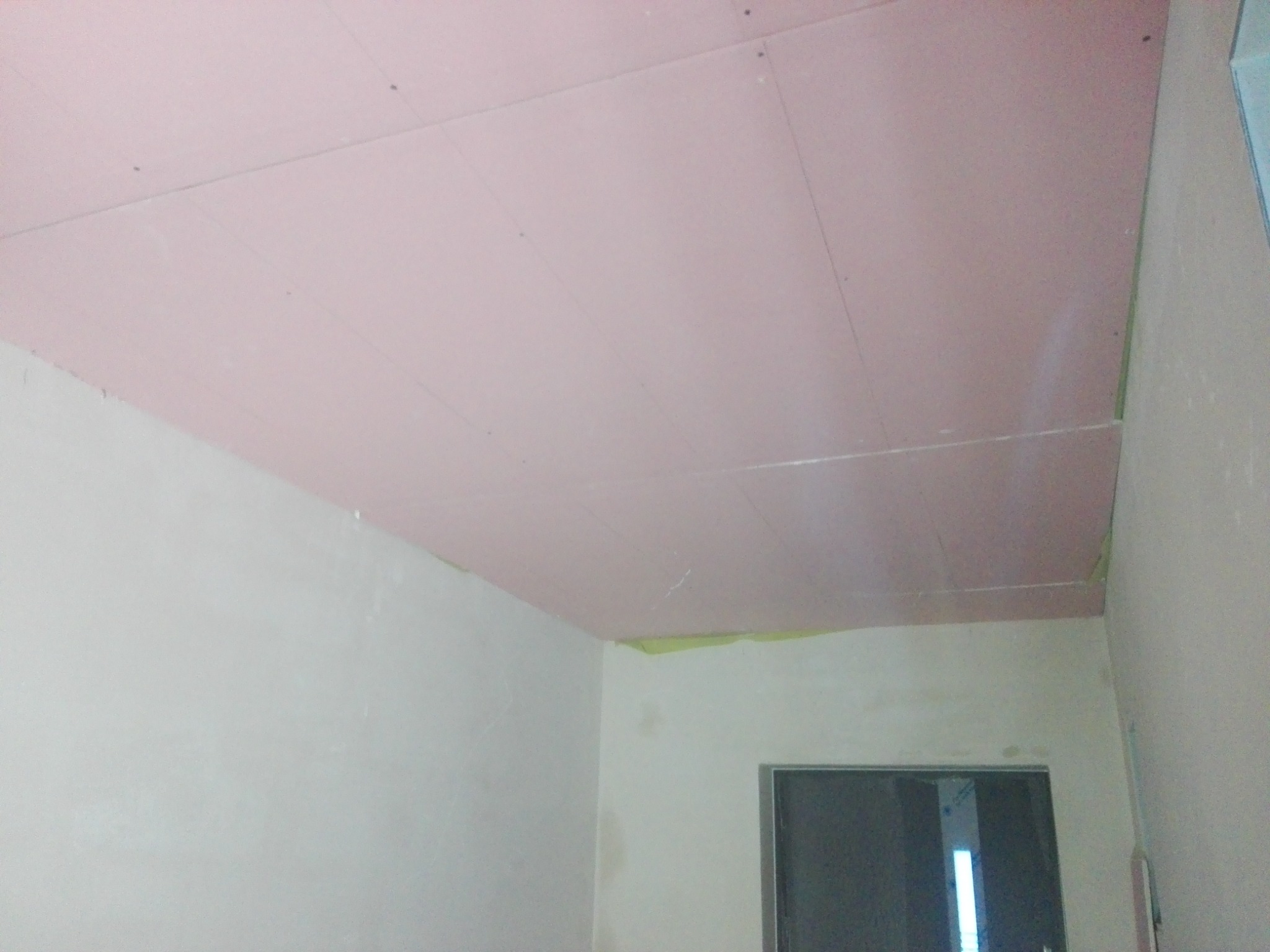 Różowa płyta karton gips zamontowana na suficie, widoczne łączenia płyt i ślady po wkrętach, ściany w trakcie przygotowania do malowania.