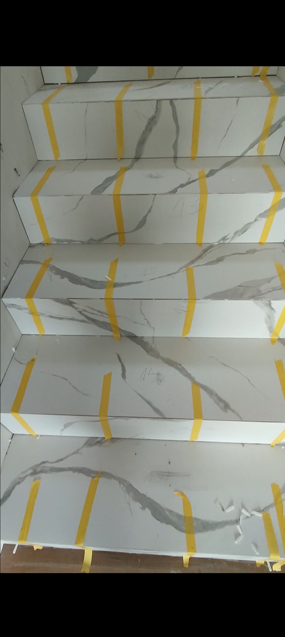 Wyłożone marmuropodobnymi płytkami schody zabezpieczone żółtą taśmą malarską podczas prac wykończeniowych.