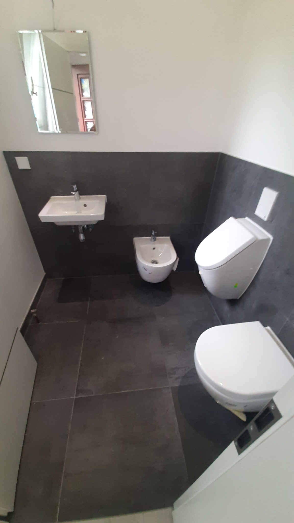 Nowoczesna łazienka z szarą glazurą, białym umywalką, bidetem i toaletą. Minimalistyczny design, lustro na ścianie. Widok z góry.