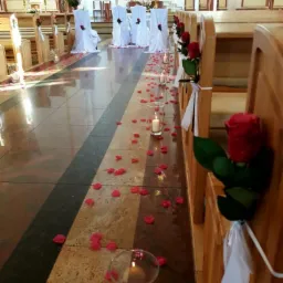 Uroczystość ślubna w kościele: przejście udekorowane płatkami róż i świecami w szklanych lampionach, ławki ozdobione różami i białymi wstążkami, krzesła w białych pokrowcach z różami.