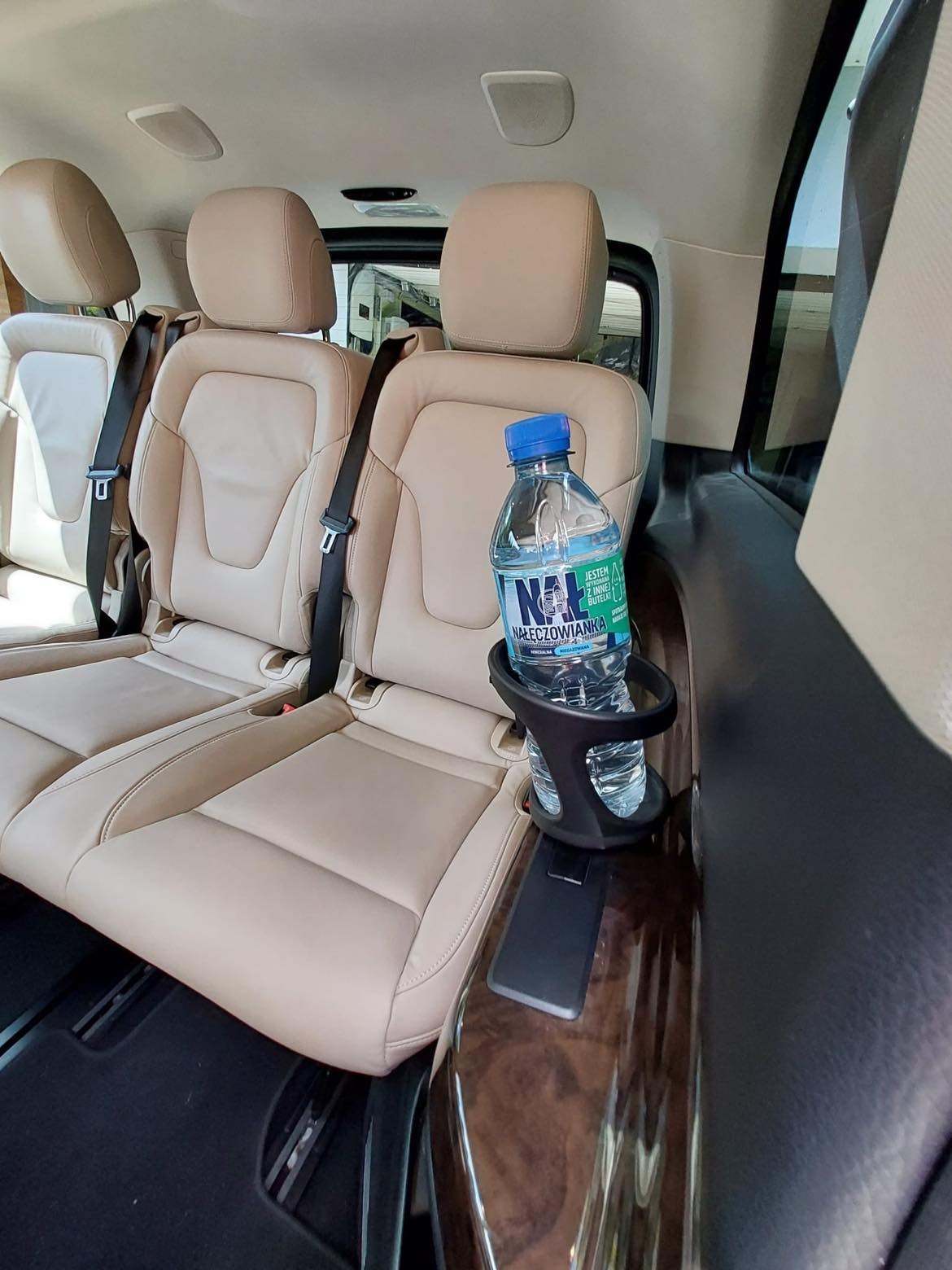 Wnętrze luksusowego busa z beżową skórzaną tapicerką, widoczna butelka wody Nałęczowianka w uchwycie na napoje.