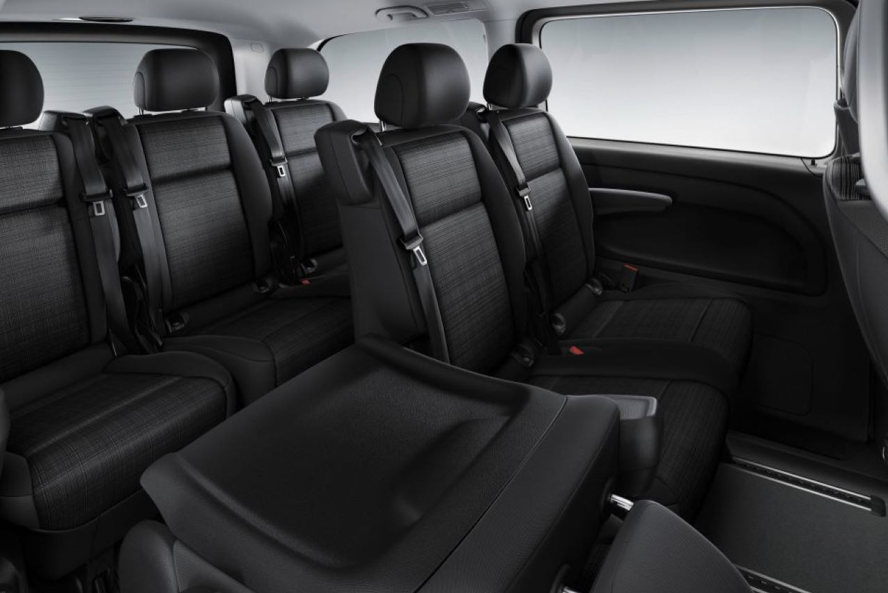 Wnętrze czarnego busa z trzema rzędami siedzeń, widoczne pasy bezpieczeństwa i przesuwne fotele na szynach.