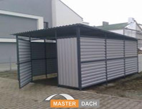 Zadaszona konstrukcja z szarej blachy falistej z czarną ramą, otwarte drzwi z jednej strony, widoczny fragment chodnika z kostki brukowej i budynki w tle.