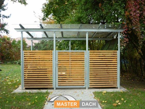 Metalowa konstrukcja z drewnianymi panelami tworząca osłonę, prawdopodobnie śmietnika, z przezroczystym zadaszeniem na tle zieleni.