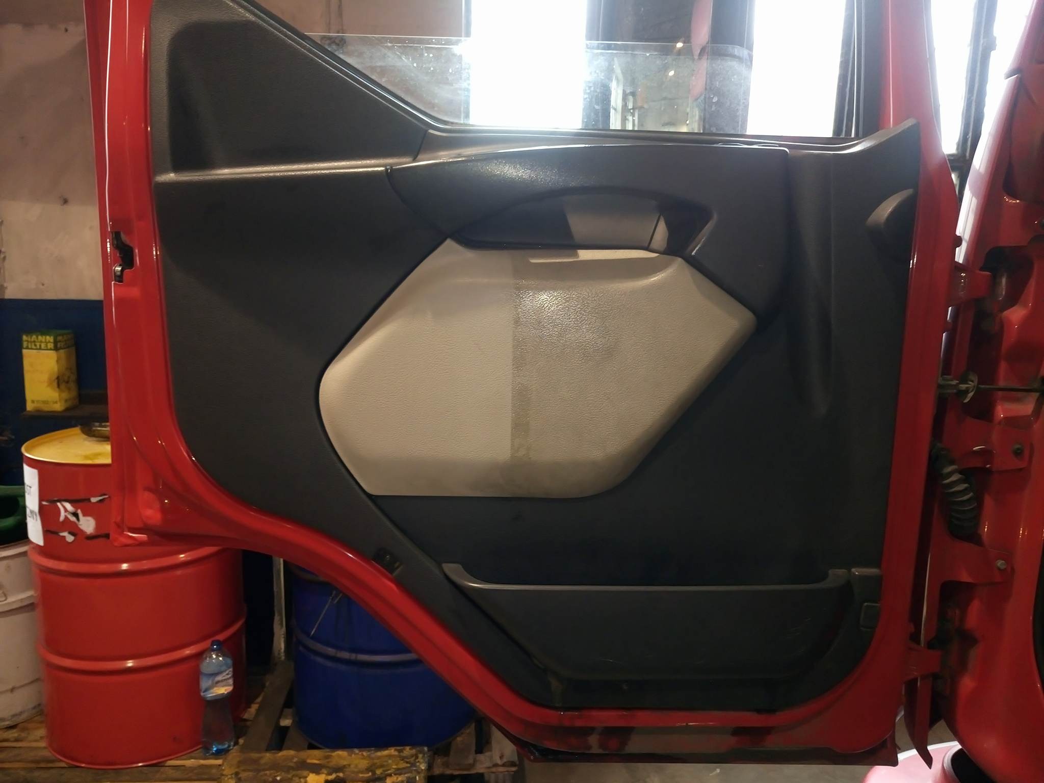 Częściowo wyczyszczona tapicerka drzwi czerwonej ciężarówki, widoczna różnica w czystości na panelu.