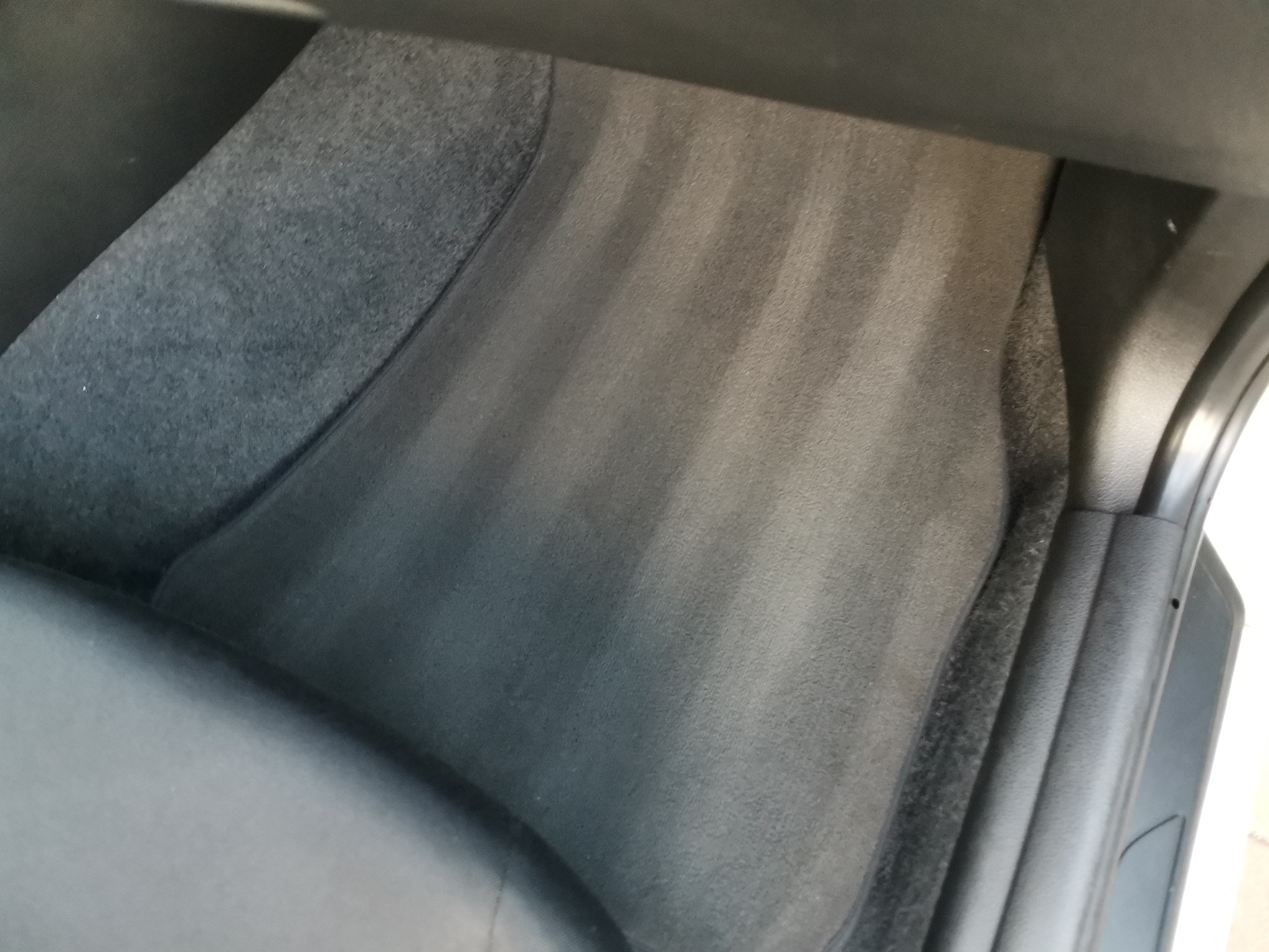 Wnętrze samochodu: wyczyszczony dywanik podłogowy z widocznymi śladami po odkurzaczu, po profesjonalnym praniu tapicerki.