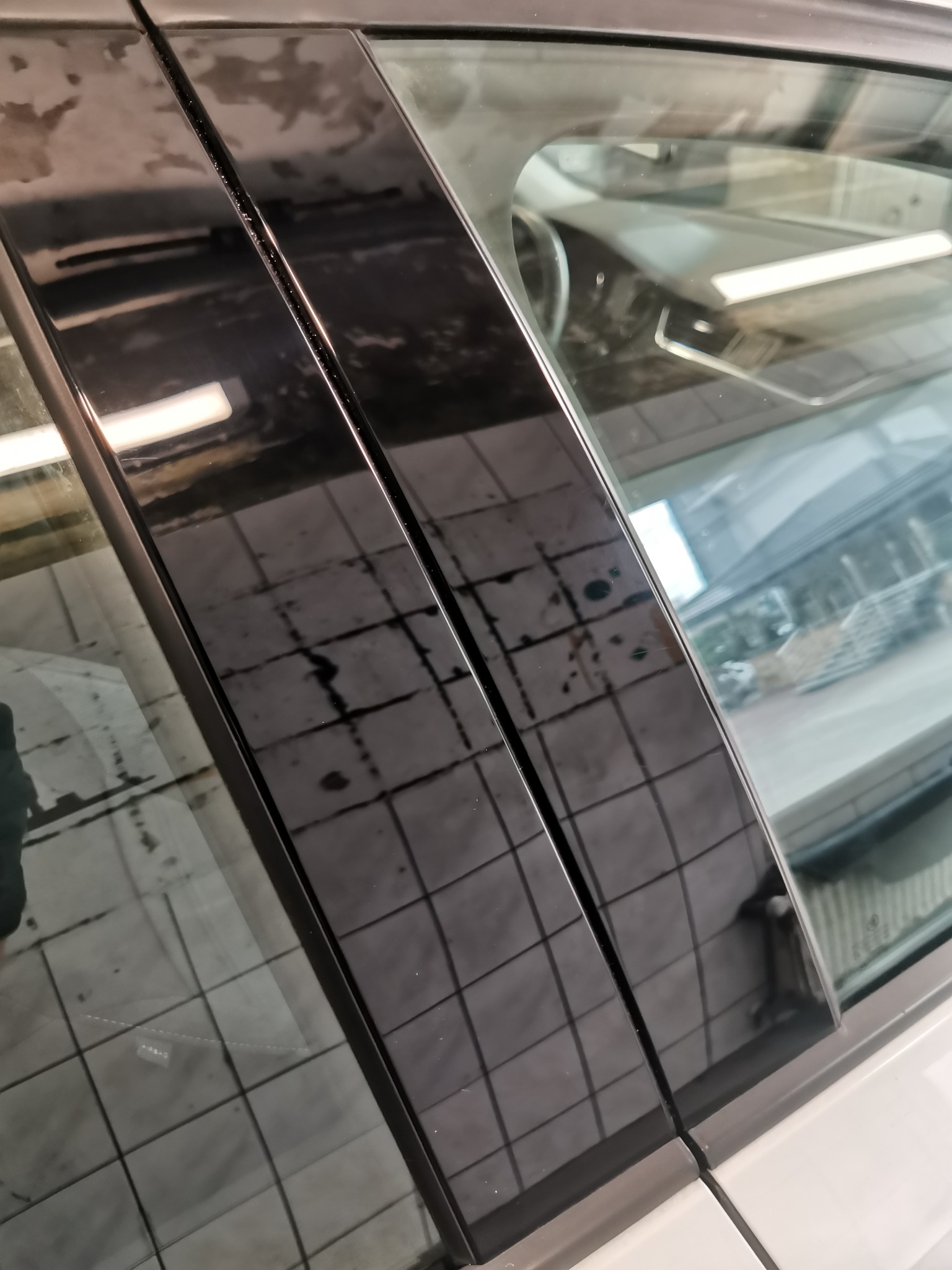 Błyszczące, czarne listwy okienne samochodu po umyciu, widoczne zacieki i odbicie kafelków podłogowych myjni.