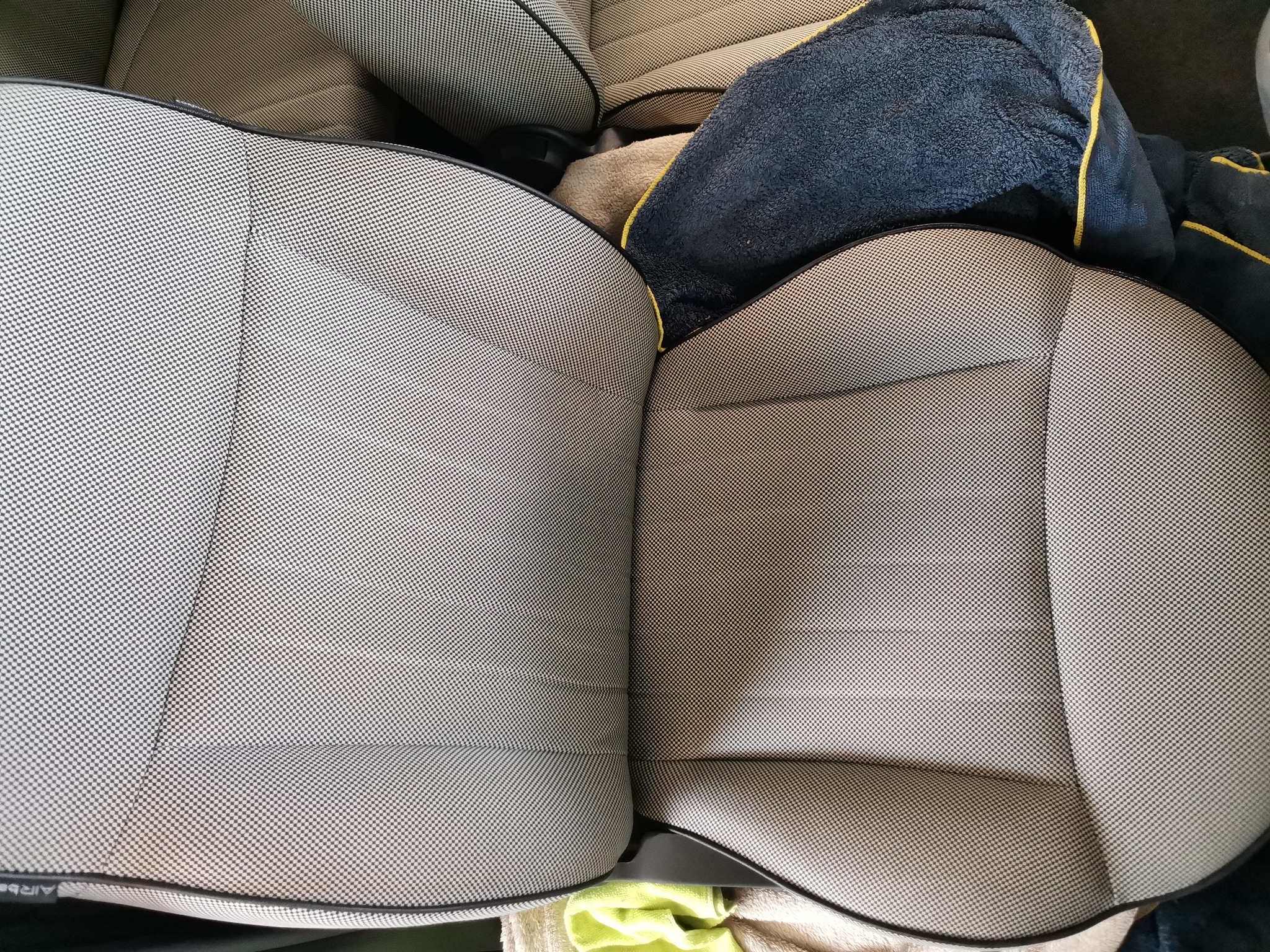Tapicerka fotela samochodowego z drobną kratką, częściowo zakryta ręcznikami po praniu, widoczne detale szwów i obicia.