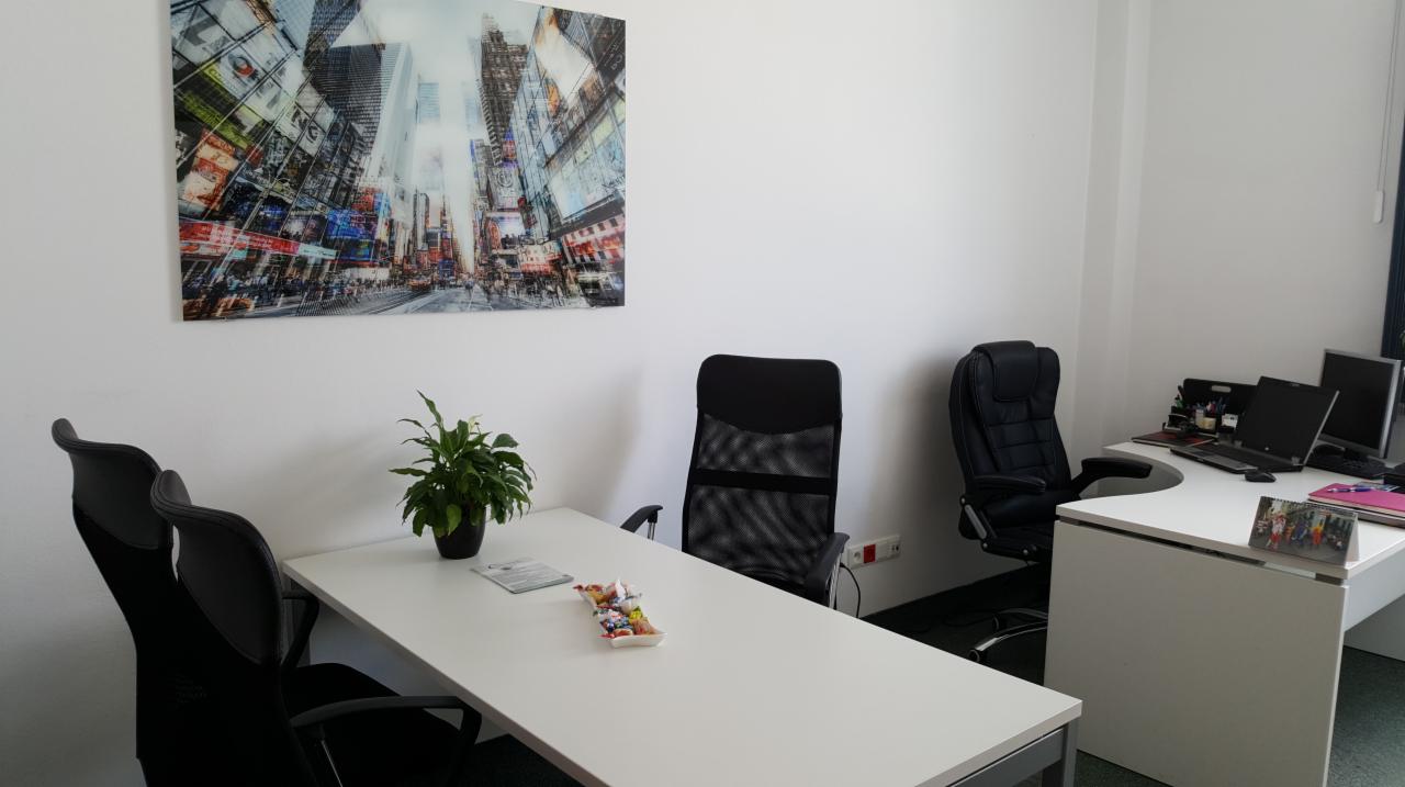 Nowoczesne biuro z białymi biurkami, czarnymi krzesłami i obrazem Times Square na ścianie, roślina doniczkowa na stole konferencyjnym.