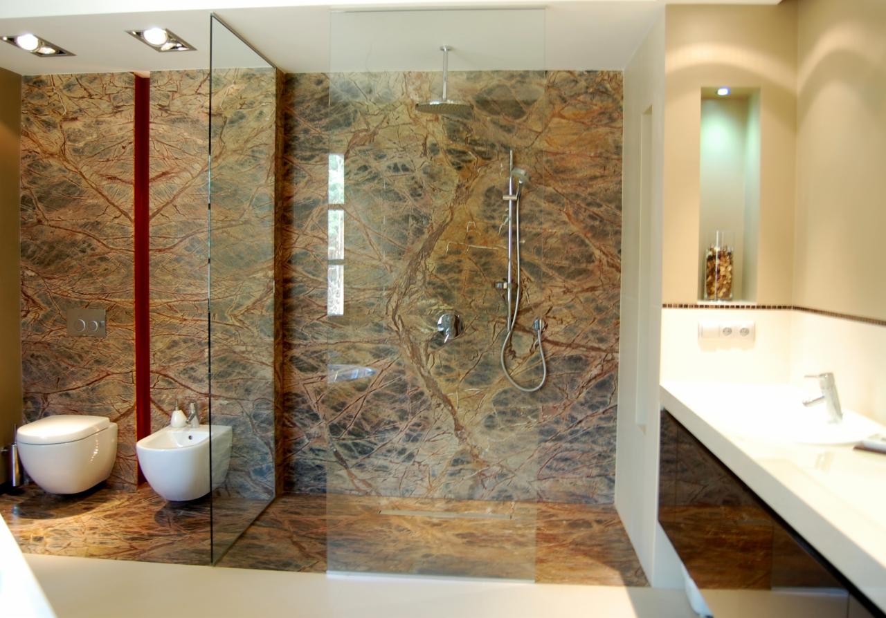 Nowoczesna łazienka z kabiną prysznicową typu walk-in wykończona brązowym marmurem Rainforest Brown, z toaletą i bidetem po lewej stronie oraz umywalką z szafką po prawej stronie.
