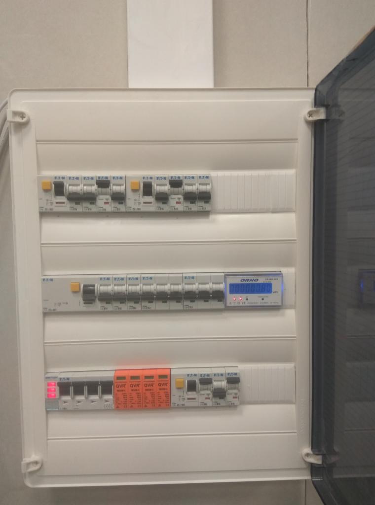 Otwarta skrzynka elektryczna z zamontowanymi bezpiecznikami, ogranicznikiem przepięć i licznikiem energii elektrycznej marki ORNO.