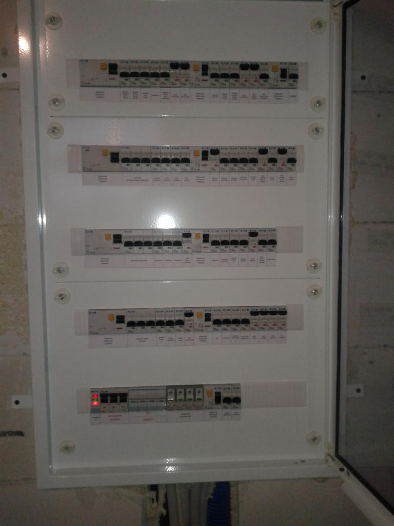 Otwarta skrzynka elektryczna z zamontowanymi bezpiecznikami i wyłącznikami różnicowoprądowymi marki Eaton, widoczne przewody w dolnej części.