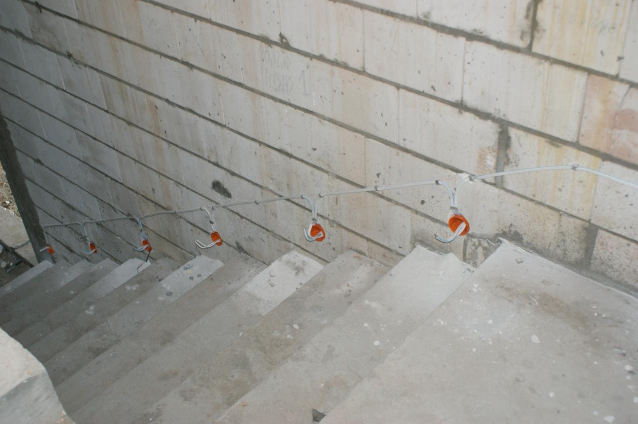 Wewnętrzne schody betonowe w surowym stanie z widoczną instalacją elektryczną w peszlach, prowadzoną wzdłuż ściany z bloczków betonowych.