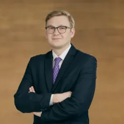 Portret młodego mężczyzny w okularach i granatowym garniturze z fioletowym krawatem na tle drewnianej ściany, Tychy.