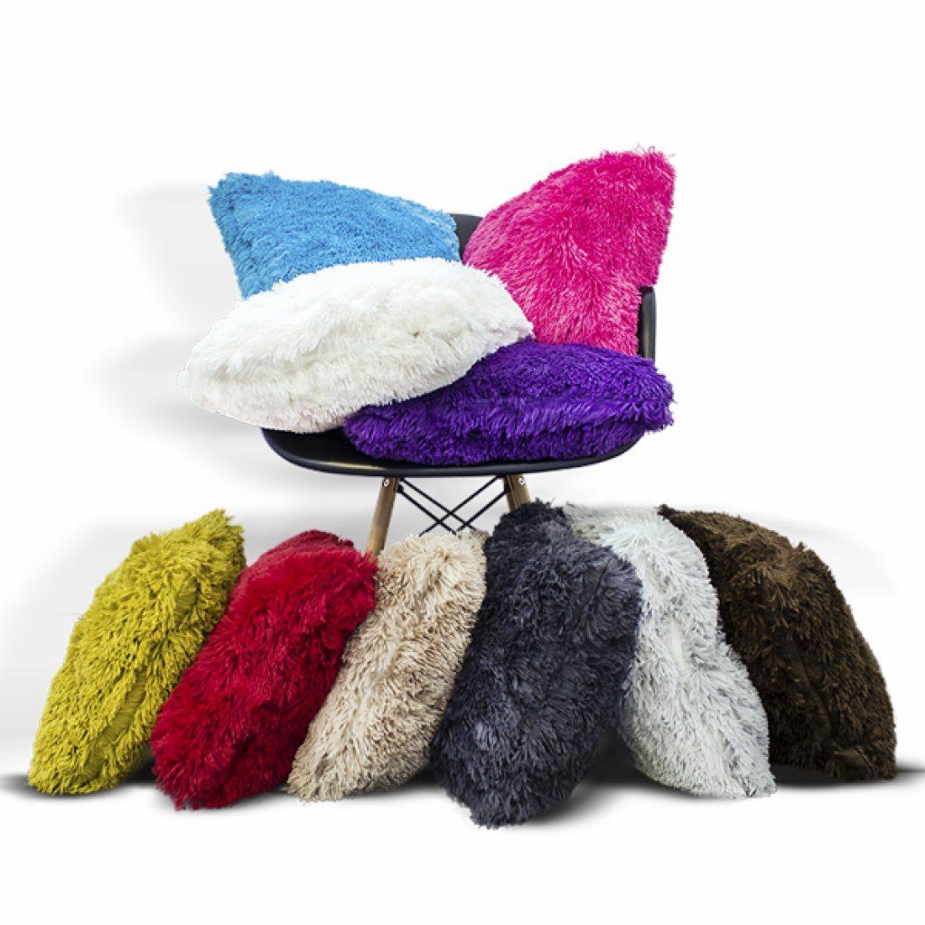 Kolekcja puszystych poduszek dekoracyjnych w różnych kolorach, ułożonych na i wokół czarnego krzesła z drewnianymi nogami, na białym tle.