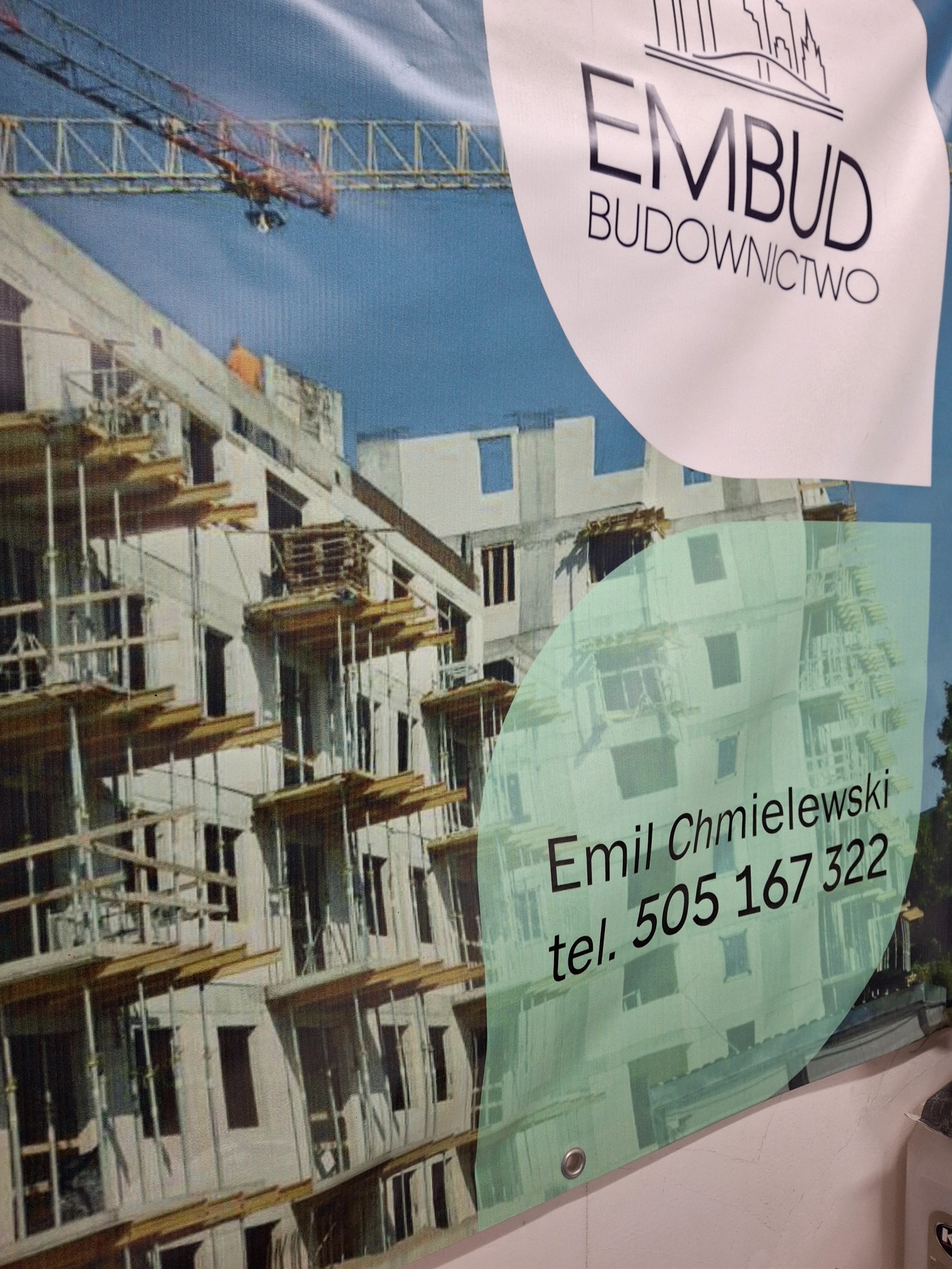 Baner reklamowy firmy budowlanej EMBUD z budynkiem w trakcie budowy i żurawiem, z danymi kontaktowymi Emil Chmielewski tel. 505 167 322.
