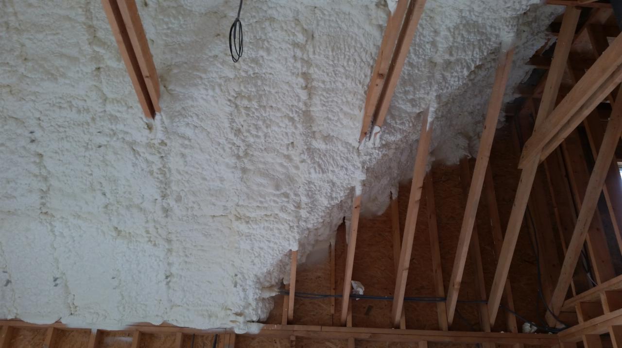 Poddasze z drewnianą konstrukcją krokwiową, ocieplone grubą warstwą białej pianki PUR, widoczne przewody elektryczne.