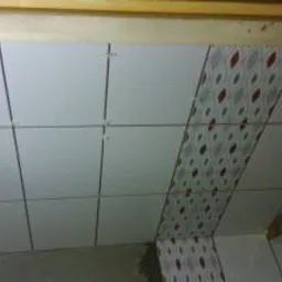 Układanie białych płytek ściennych z dekoracyjnym pasem w łazience w Będzinie, widoczne krzyżyki dystansowe i poziomica.