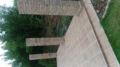 Wyłożona jasnymi płytkami ściana z wystającymi ceglanymi filarami na tle zieleni.