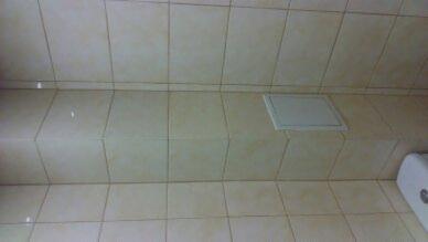 Beżowe płytki ceramiczne na ścianie łazienki z widocznym włazem rewizyjnym i fragmentem białego bojlera.