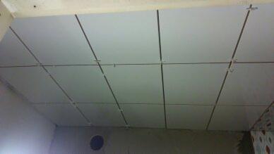 Montaż kasetonów na suficie z widocznymi krzyżykami dystansowymi w trakcie prac wykończeniowych.