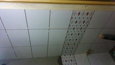 Układanie białych płytek ściennych z dekoracyjnym pasem w łazience w Będzinie, widoczne krzyżyki dystansowe i poziomica.