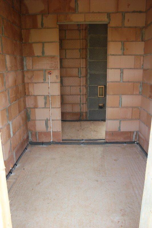 Surowy stan wnętrza z widocznymi przewodami elektrycznymi ułożonymi wzdłuż ścian, ceglane ściany w trakcie budowy, widoczne puszki instalacyjne.