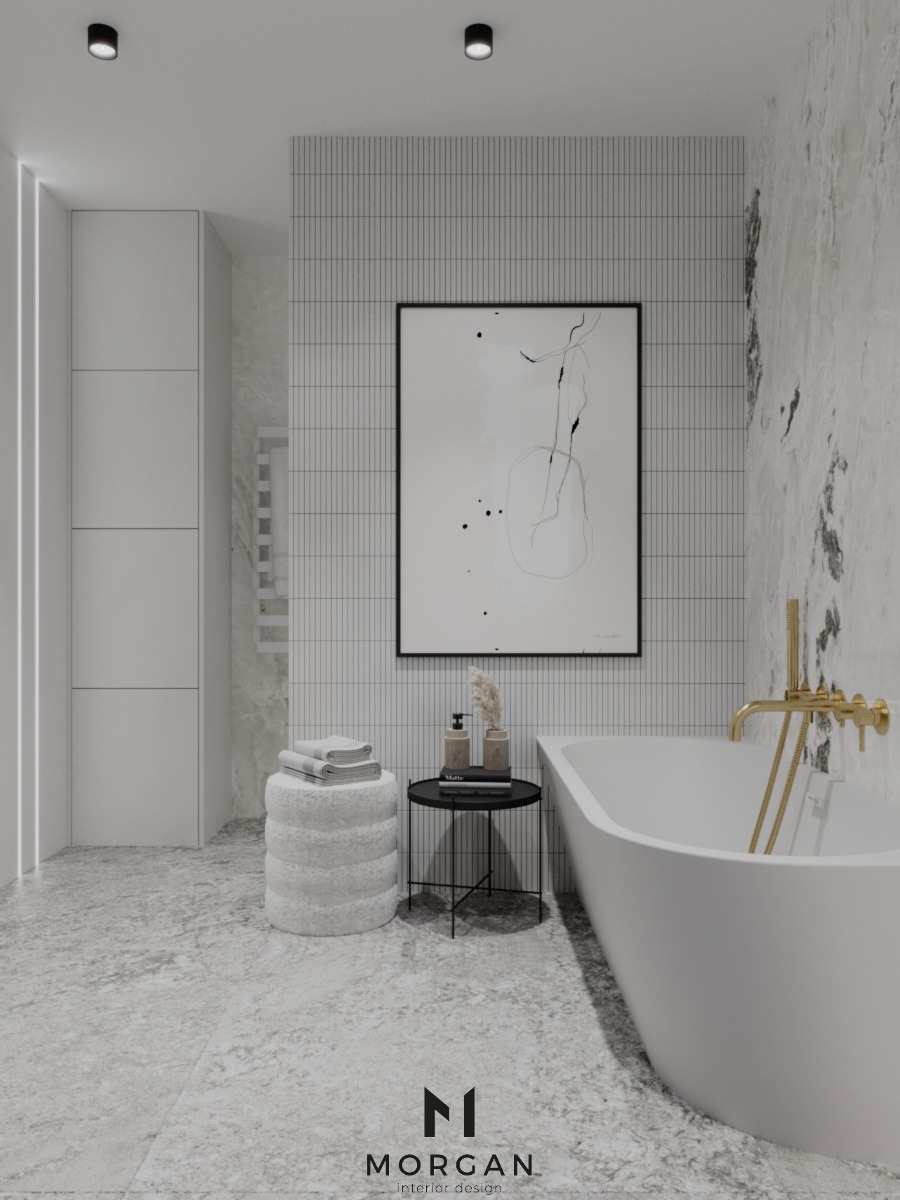 Minimalistyczna łazienka w odcieniach bieli i szarości z wolnostojącą wanną, złotą armaturą, abstrakcyjnym obrazem w czarnej ramie, pufą z ręcznikami i małym stolikiem z kosmetykami.