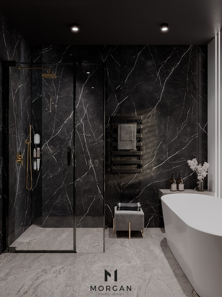 Nowoczesna łazienka z czarnymi marmurowymi ścianami, kabiną prysznicową typu walk-in z złotą armaturą, grzejnikiem drabinkowym na ręczniki, wolnostojącą białą wanną i szarym taboretem.