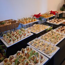 Global Chefs Mariusz Powierża - Bogato zastawiony stół cateringowy z różnorodnymi przekąskami: roladki, koreczki, pieczywo w koszyku. Dekoracje świąteczne z poinsecji. Idealne na firmowe przyjęcie.