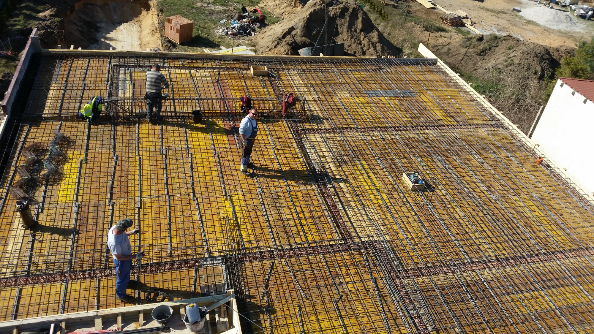 Zbrojenie płyty fundamentowej z żółtym szalunkiem, widok z góry, pracownicy w trakcie montażu.
