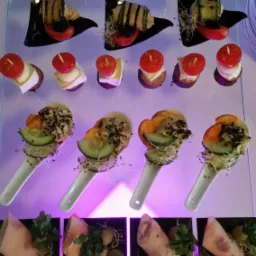 Różnorodne przekąski na szklanym stojaku: roladki z szynki z ziołami, koreczki z pomidorkami i serem, roladki z grillowanej cukinii na czarnych talerzykach, oraz przystawki na białych łyżkach...