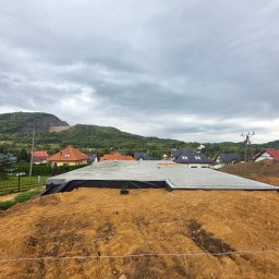 PHU WILBUD Krzysztof Wilczyński - Wylana płyta fundamentowa z izolacją w Złotoryi, widok z góry na tle zabudowy mieszkalnej i zalesionego wzgórza pod pochmurnym niebem.