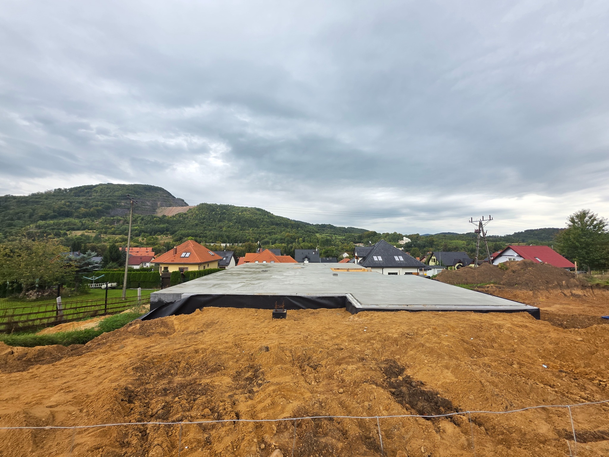 Wylana płyta fundamentowa z izolacją w Złotoryi, widok z góry na tle zabudowy mieszkalnej i zalesionego wzgórza pod pochmurnym niebem.
