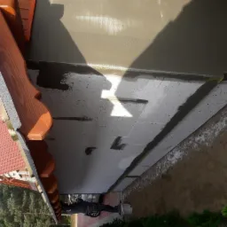 Ocieplanie elewacji budynku jednorodzinnego: styropian z nałożoną siatką i klejem, widoczny fragment dachu z drewnianymi zdobieniami.