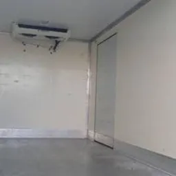 Pusta, biała przestrzeń ładunkowa chłodni z widocznym agregatem chłodniczym pod sufitem i drzwiami po prawej stronie.