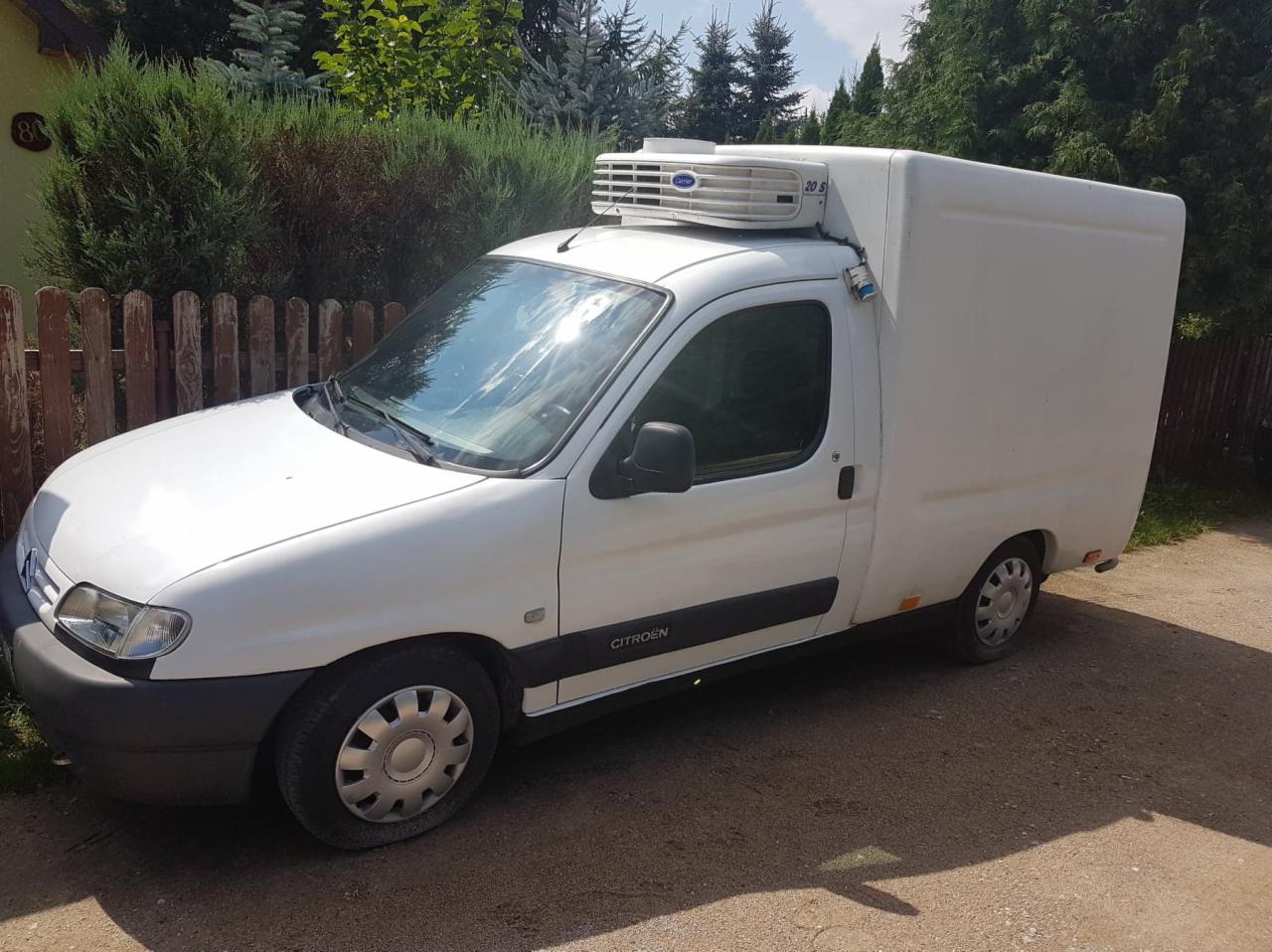 Biały samochód dostawczy typu furgon chłodnia marki Citroen Berlingo zaparkowany na żwirowej drodze, z widocznym agregatem chłodniczym Carrier na dachu.