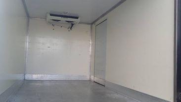 Pusta, biała przestrzeń ładunkowa chłodni z widocznym agregatem chłodniczym pod sufitem i drzwiami po prawej stronie.