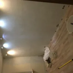 Świeżo wykończona powierzchnia sufitu z zamontowanymi punktowymi źródłami światła, widoczne narzędzia i materiały budowlane na podłodze