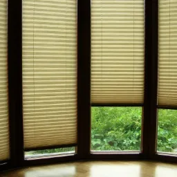 Beżowe, plisowane osłony okienne zamontowane w oknach wykuszowych z widokiem na bujną zieleń ogrodu.