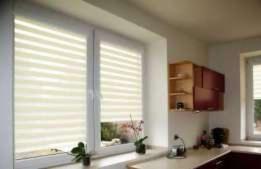 Zamknięte jasne osłony okienne z poziomymi pasami w oknie kuchennym, widok na blat i szafki.