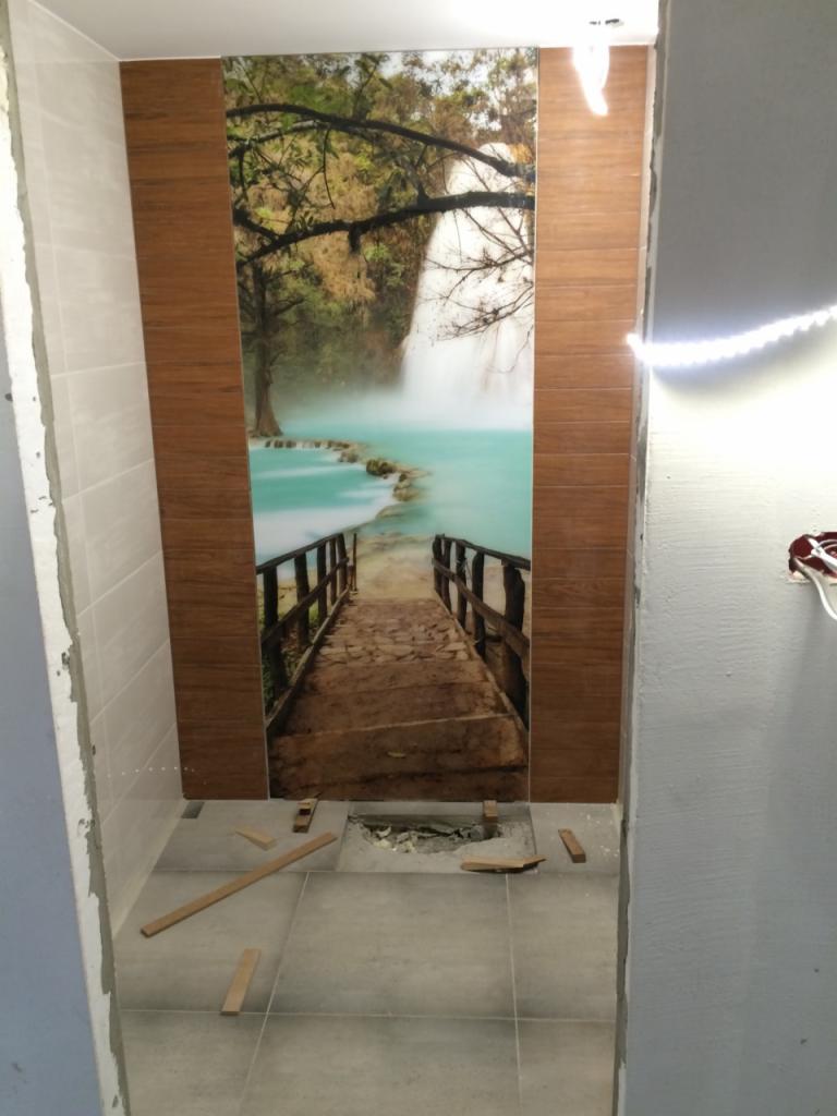 Montaż płytek imitujących drewno z nadrukiem wodospadu w łazience, widoczne niedokończone prace na podłodze.