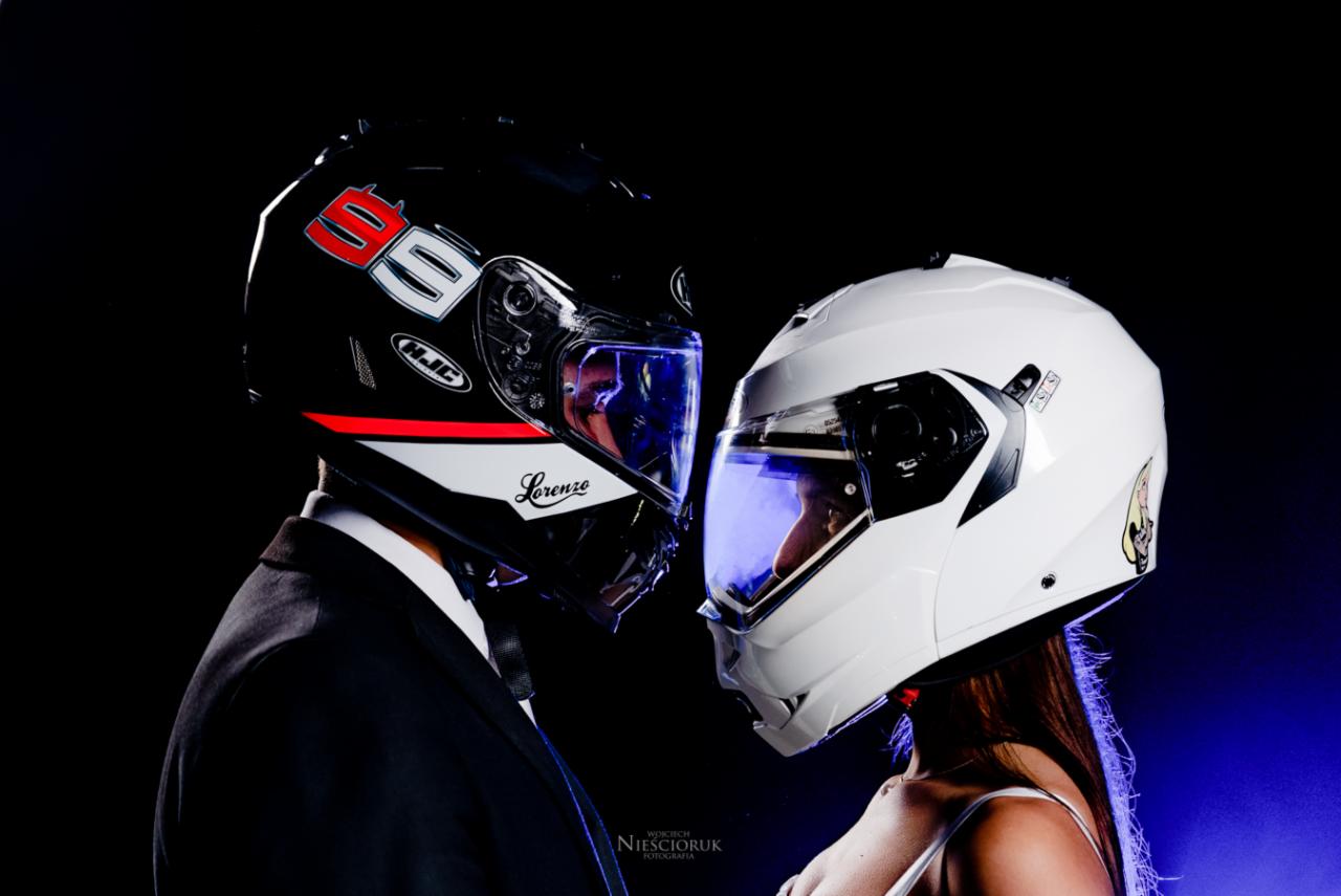Para w kaskach motocyklowych, on w garniturze, ona w białej sukience, zbliżają się do siebie, na kasku Lorenzo widoczny napis 'Lorenzo', w tle ciemne tło z niebieską poświatą.